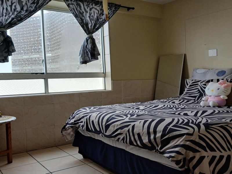 A bedroom featuring tiled flooring and lower wall tiling, with a large window providing natural light and an urban view.