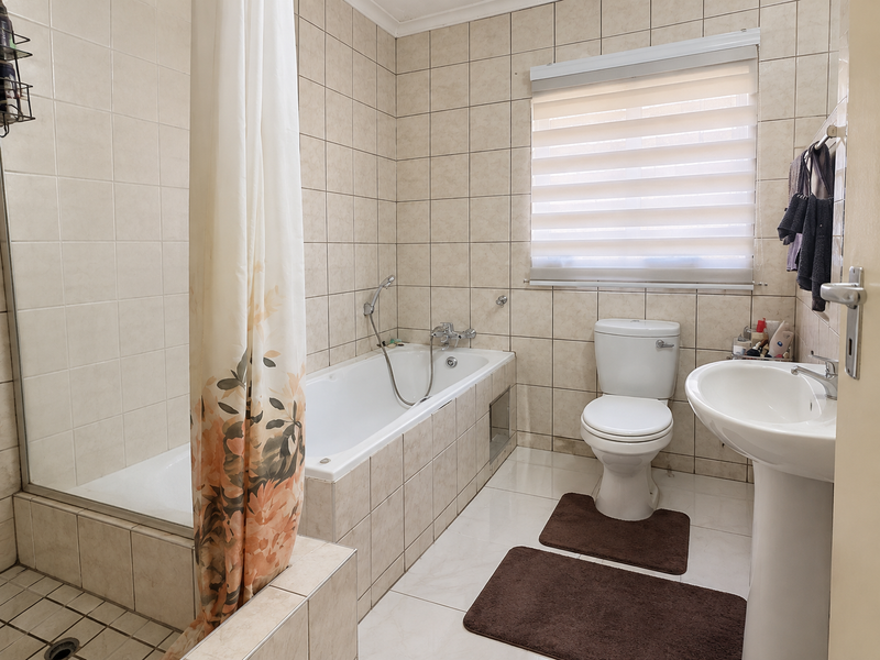 A functional bathroom featuring tiled walls and flooring, a combined bathtub and shower, a pedestal basin, and a standard toilet.