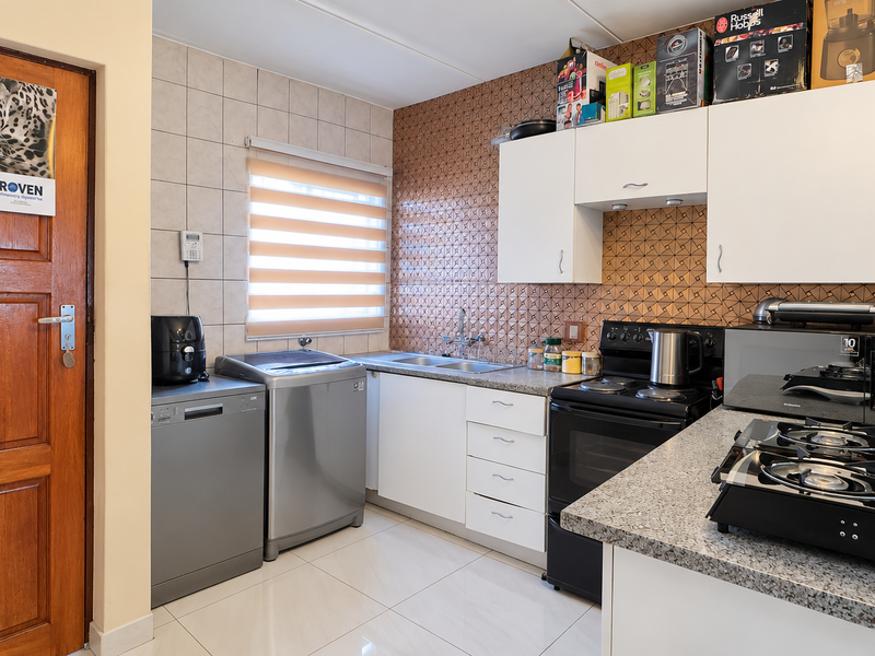 A functional kitchen featuring white cabinetry, granite countertops, a double sink, and a tiled backsplash, with space for under-counter appliances.