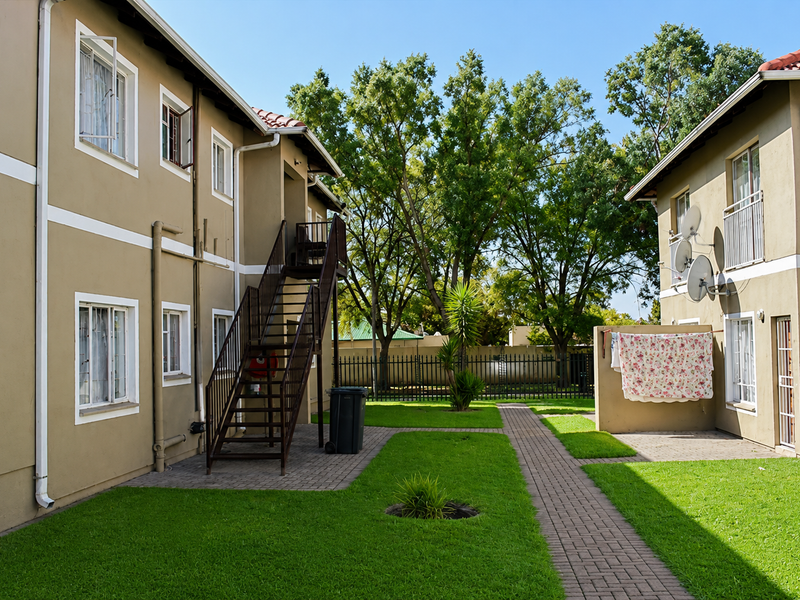 Rear view of the apartment complex featuring a communal garden, paved walkways, and external metal staircases providing access to upper levels.