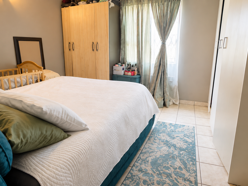 A functional bedroom featuring built-in cupboards, tiled flooring, and a window with security gate, offering a practical layout for comfortable living.