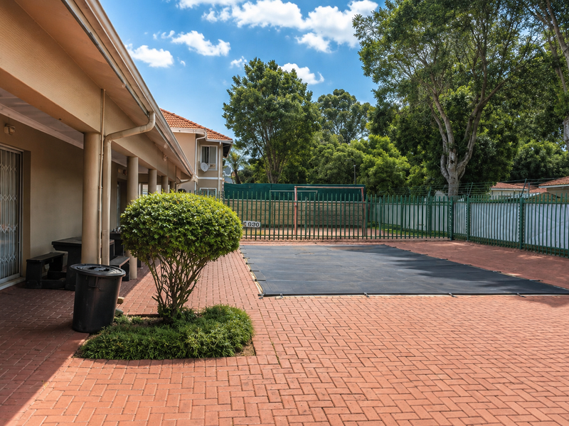 Outdoor pool area featuring a covered patio, paved terrace, and secure perimeter fencing, providing a functional space for outdoor relaxation.