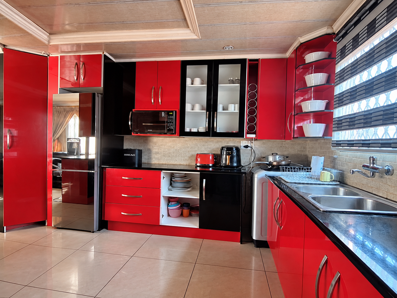 A vibrant kitchen featuring high-gloss red and black cabinetry, a double sink with mixer tap, tiled backsplash, and integrated microwave.