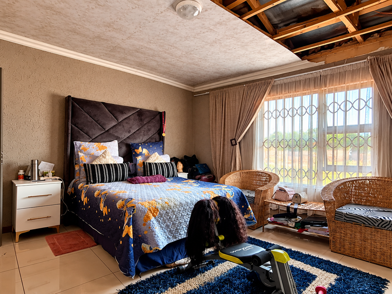 Spacious bedroom featuring tiled flooring and security bars on the window, currently requiring ceiling repairs and finishing.