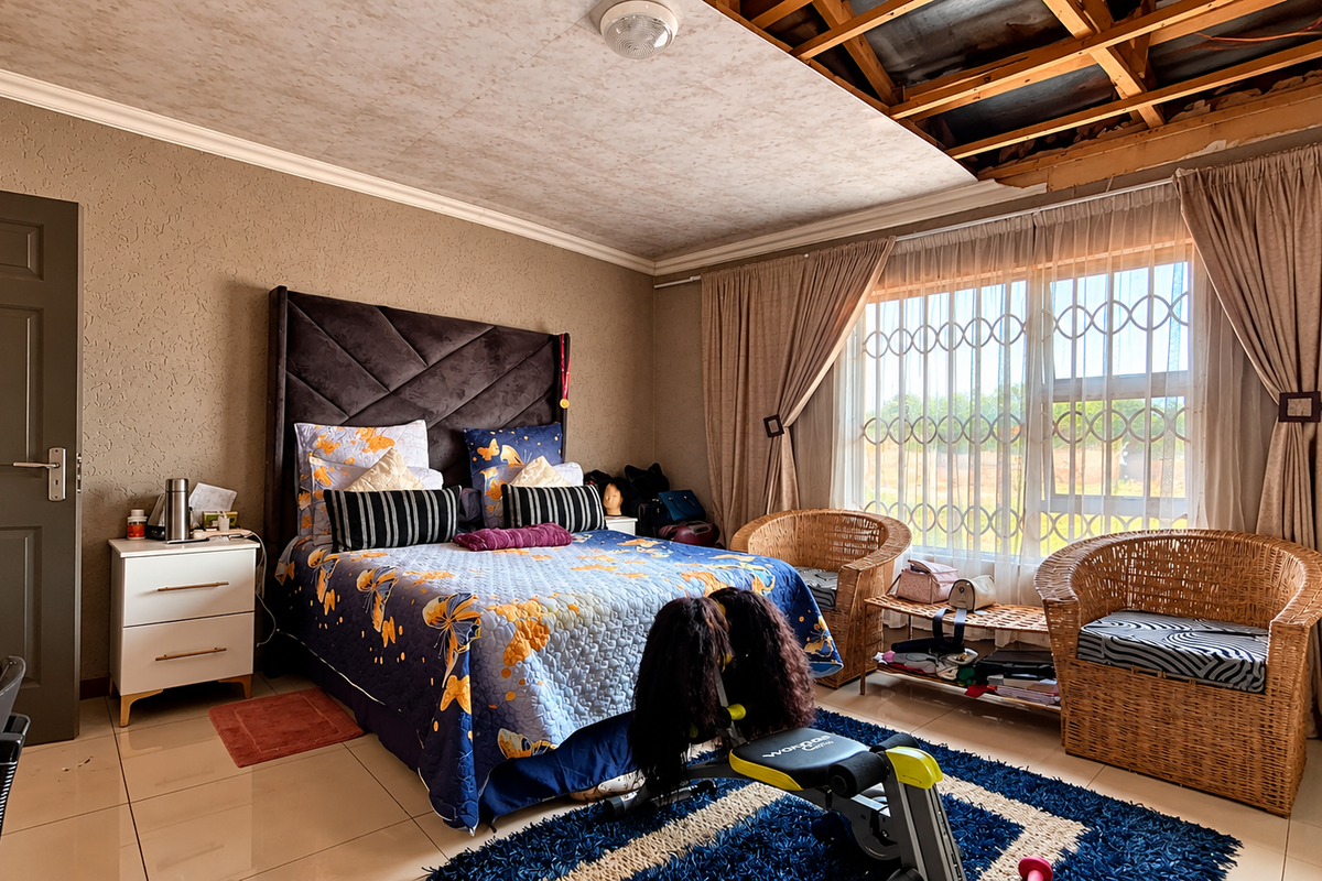Spacious bedroom featuring tiled flooring and security bars on the window, currently requiring ceiling repairs and finishing.
