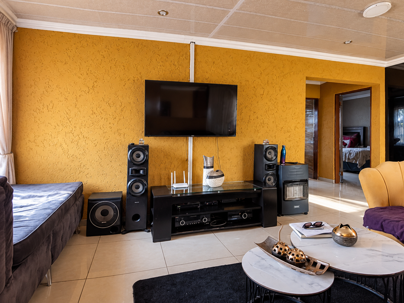 A living room featuring textured yellow walls, tiled flooring, and recessed ceiling lighting, with a clear view into an adjacent bedroom.