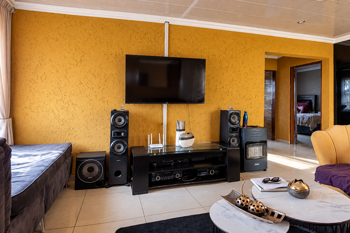 A living room featuring textured yellow walls, tiled flooring, and recessed ceiling lighting, with a clear view into an adjacent bedroom.