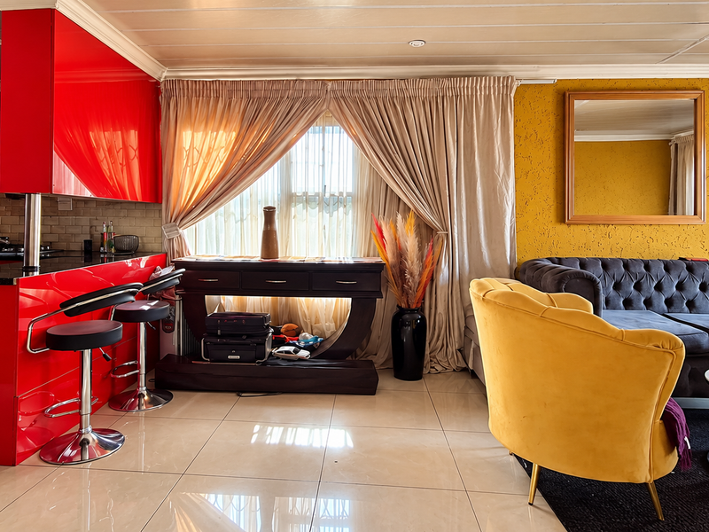 Open-plan living area featuring a vibrant red kitchen with granite countertops and a contrasting yellow textured feature wall, creating a bold, modern aesthetic.