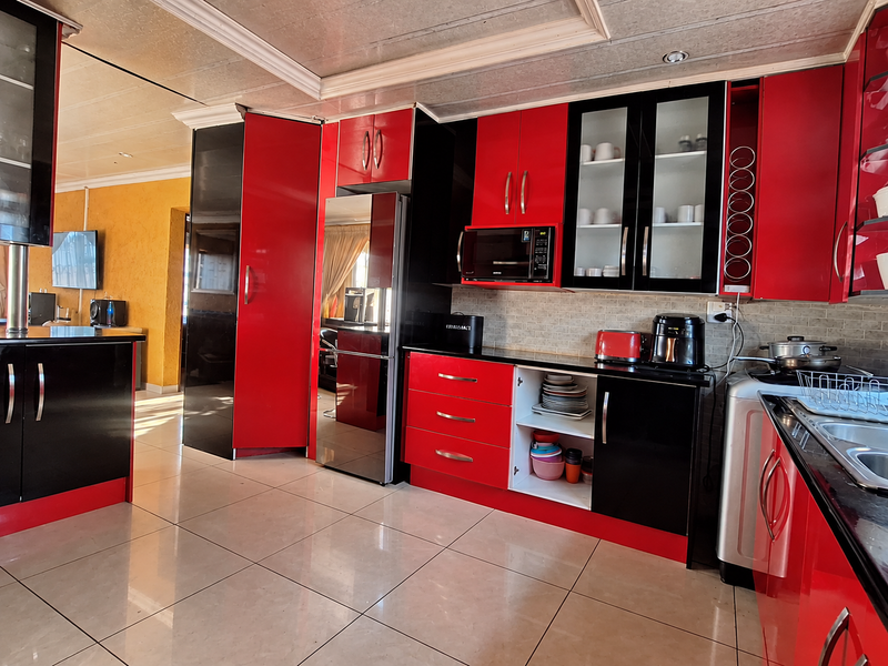 Modern kitchen featuring high-gloss red and black cabinetry, tiled flooring, built-in microwave, and glass-fronted display units with integrated lighting.