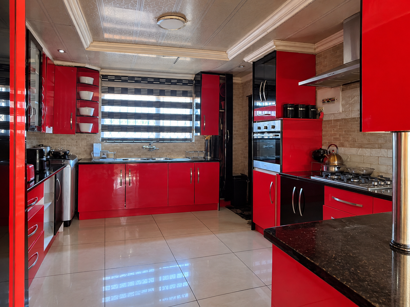 A modern kitchen featuring high-gloss red cabinetry, granite countertops, integrated stainless steel appliances, and tiled flooring with a neutral backsplash.