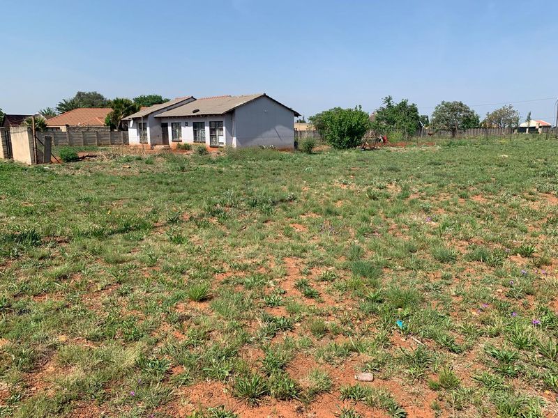 A view of a residential plot featuring a single-story dwelling with a tiled roof and surrounding perimeter boundary walls.