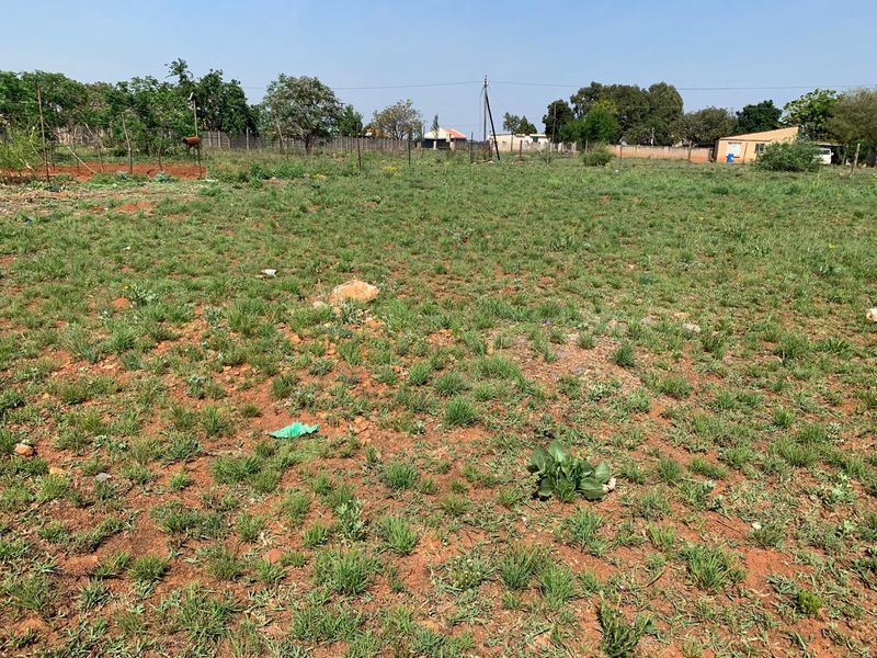 A vacant residential plot featuring natural grass cover, enclosed by wire fencing with a utility pole visible in the background.