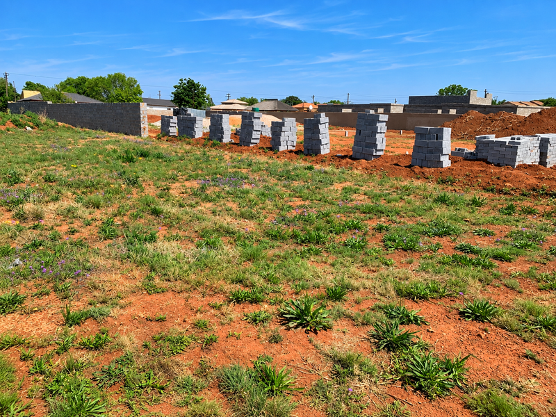 A vacant residential plot featuring a boundary wall and stacks of concrete masonry units ready for construction.