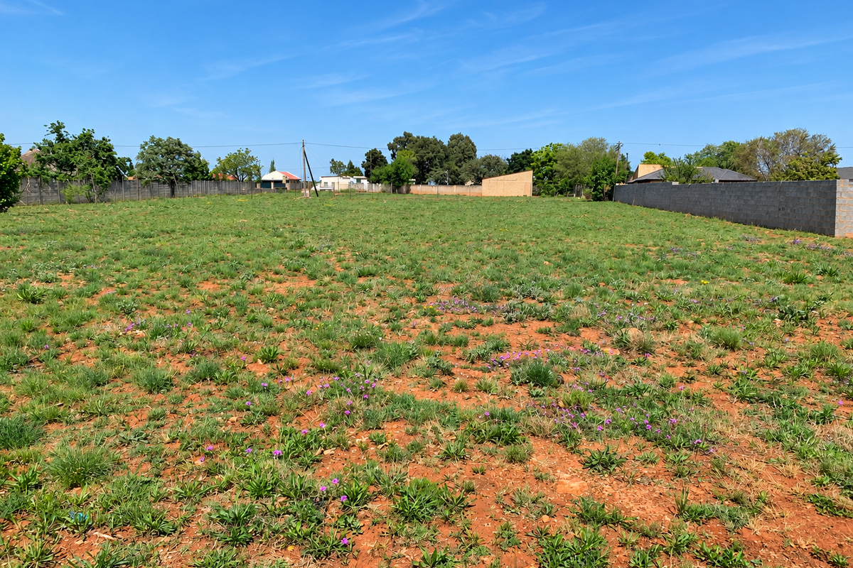 A vacant residential plot featuring natural ground cover and enclosed by perimeter boundary walls on multiple sides.