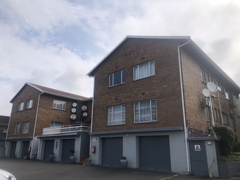Front elevation of a multi-story face brick apartment complex featuring multiple roller shutter garage doors and security-fitted windows.