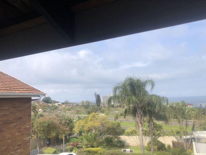 An elevated view overlooking the surrounding neighbourhood, lush greenery, and distant ocean horizon from the property.