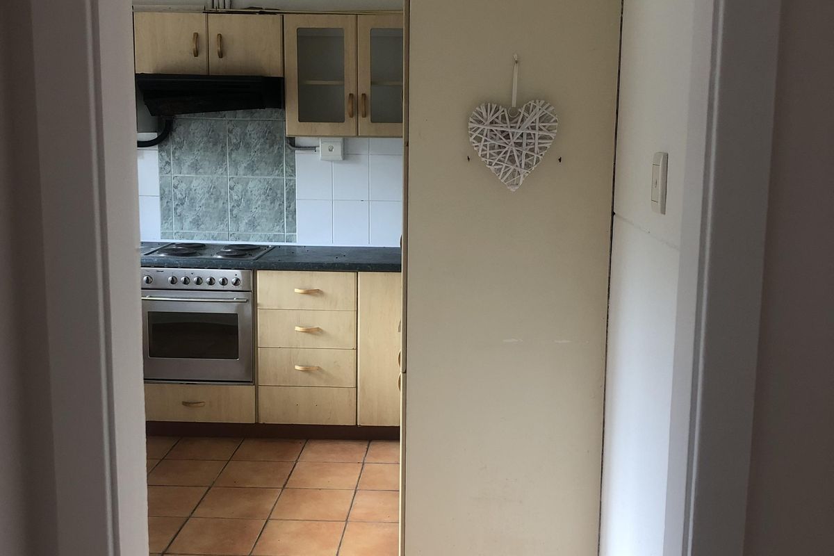 A functional kitchen featuring built-in cabinetry, an electric oven and hob, extractor fan, and tiled flooring, presenting an opportunity for cosmetic updates.