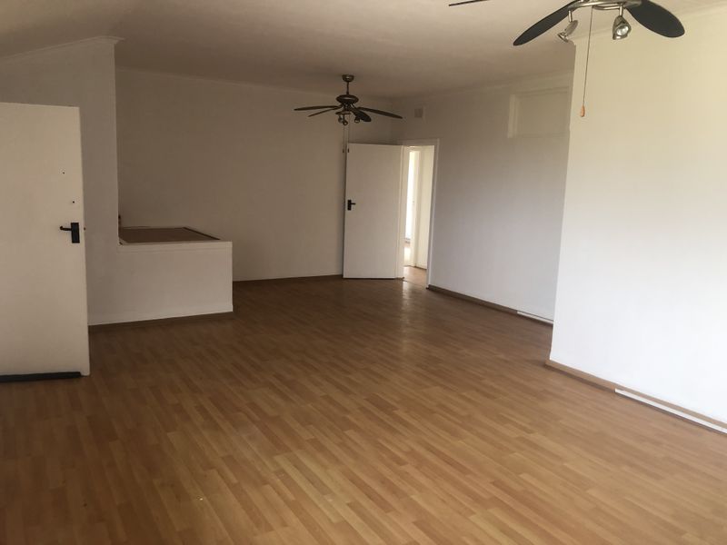 An empty, open-plan living area featuring laminate flooring, ceiling fans, and neutral white walls, providing a blank canvas for interior design.