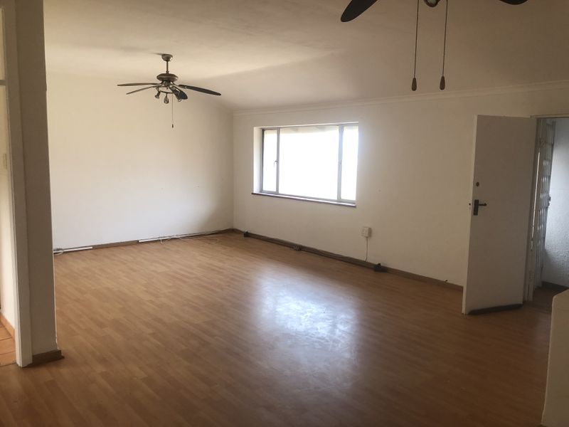 A spacious, empty living room featuring laminate flooring, ceiling fans, and neutral walls, offering a blank canvas for interior design.