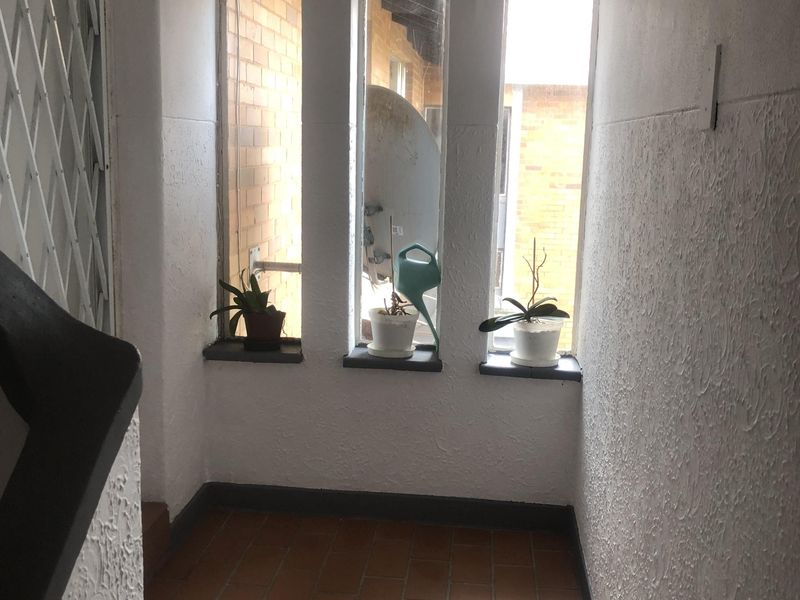 A functional hallway area featuring tiled flooring, textured wall finishes, and a security gate, providing access to the property.