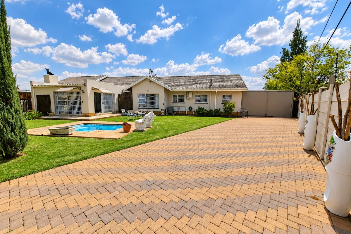 Rear view of the property featuring a paved driveway, a swimming pool, and a well-maintained lawn area.