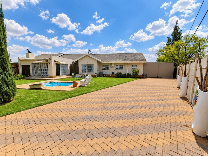 Rear view of the property featuring a paved driveway, a swimming pool, and a well-maintained lawn area.