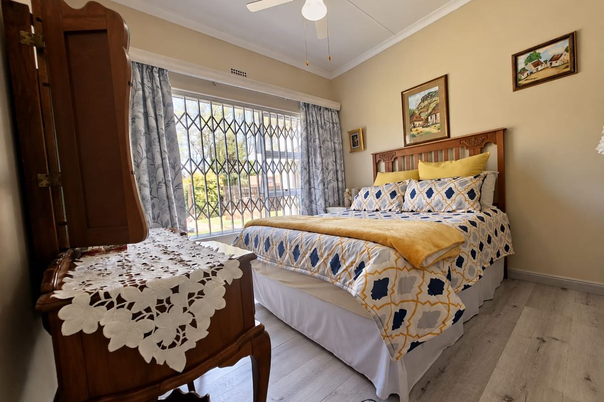 A well-maintained bedroom featuring laminate flooring, a ceiling fan, and a secure window with a fitted security gate.