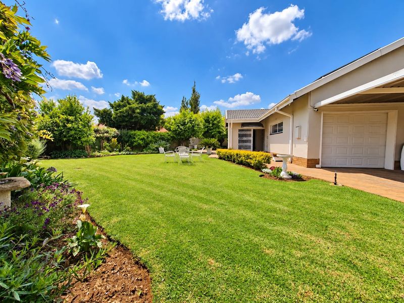 A well-maintained rear garden featuring a lush lawn, landscaped flower beds, and a paved patio area adjacent to the garage and home entrance.
