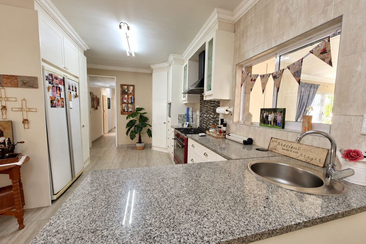 A well-maintained kitchen featuring granite countertops, built-in cabinetry, a gas stove with extractor fan, and a convenient pass-through window to the adjacent living area.