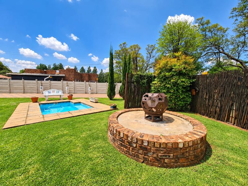 Outdoor entertainment area featuring a swimming pool with paved surround, a circular brick fire pit, and established garden landscaping.