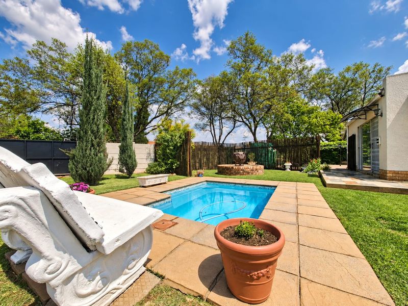 A well-maintained backyard featuring a swimming pool with paved surround, established garden, and brick boundary walling.