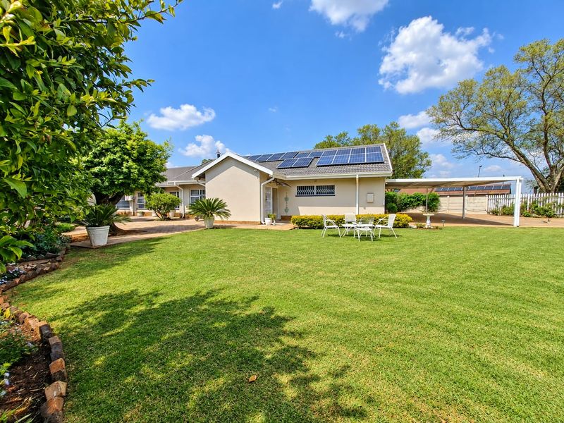A well-maintained rear exterior view featuring a spacious lawn, paved patio area, and roof-mounted solar panels.