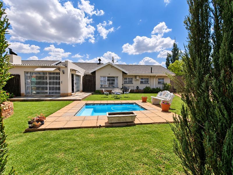 Rear view of the property featuring a well-maintained garden, a swimming pool with tiled surround, and a paved patio area.