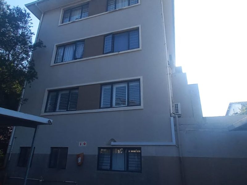 Rear elevation of a multi-story flat building featuring aluminium window frames and covered carport parking areas.