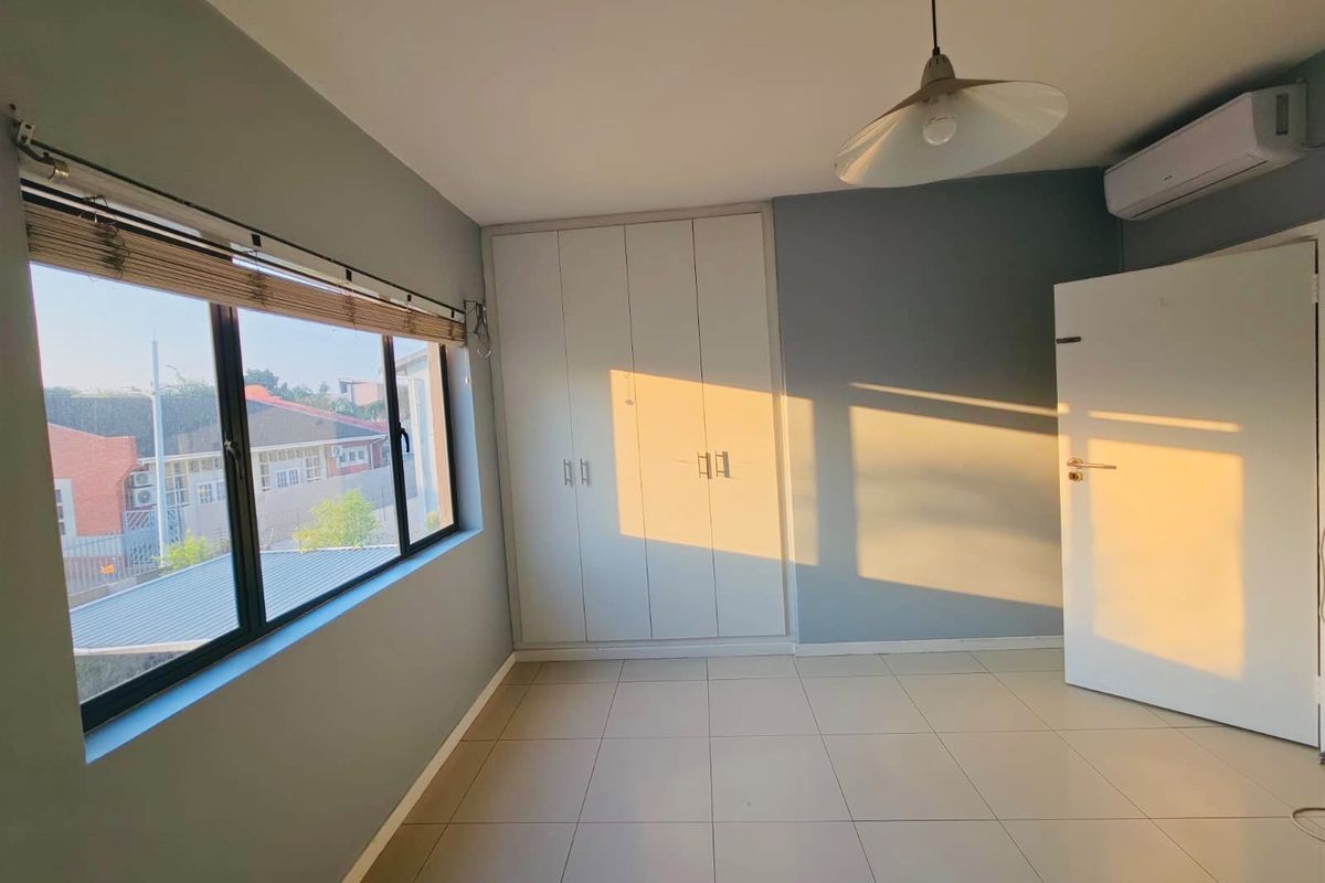 A bright, empty bedroom featuring tiled flooring, built-in cupboards, and a wall-mounted air conditioning unit, illuminated by warm natural light.