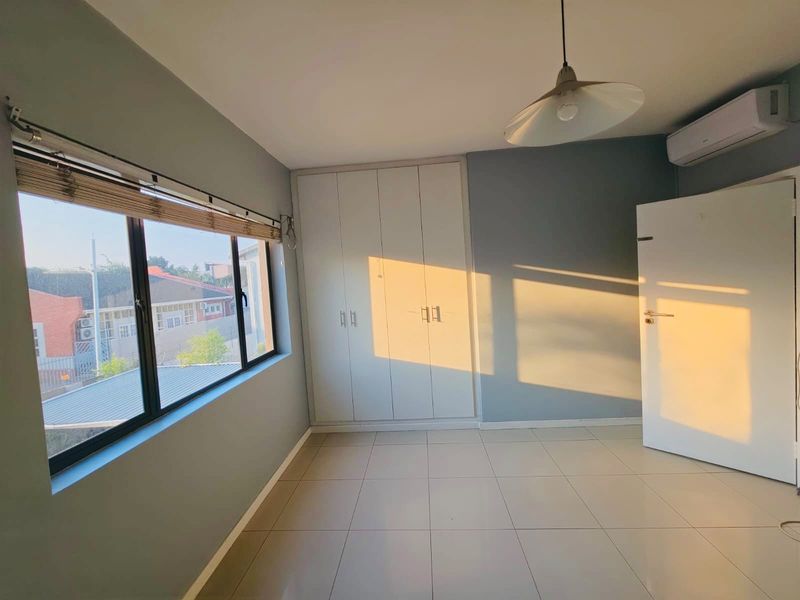 A bright, empty bedroom featuring tiled flooring, built-in cupboards, and a wall-mounted air conditioning unit, illuminated by warm natural light.