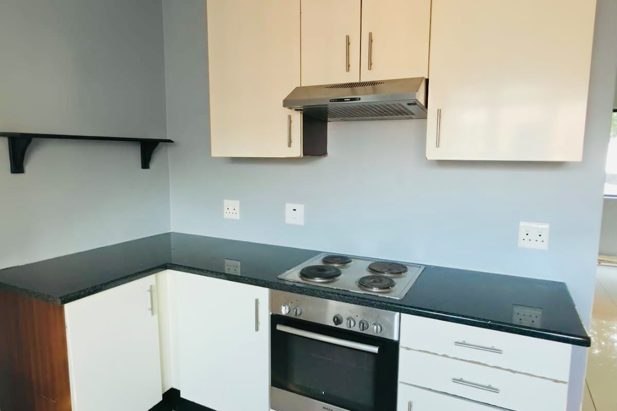 A compact kitchen featuring built-in cabinetry, granite countertops, an integrated oven, and an electric hob, finished with tiled flooring.