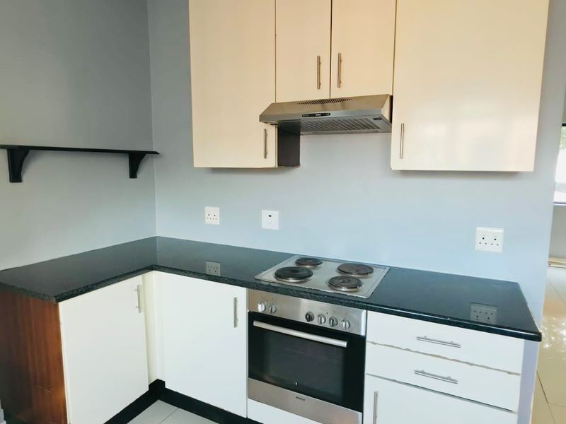 A compact kitchen featuring built-in cabinetry, granite countertops, an integrated oven, and an electric hob, finished with tiled flooring.