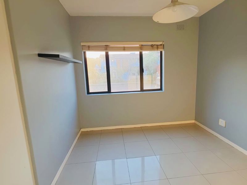 A bright, empty bedroom featuring neutral wall paint, large tiled flooring, a built-in floating shelf, and a modern pendant light fixture.