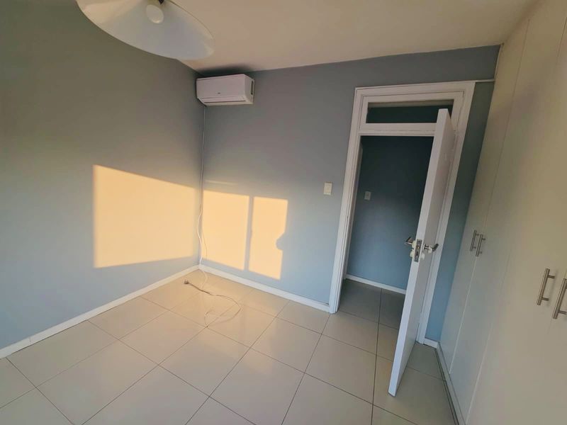 A clean, empty bedroom featuring tiled flooring, built-in cupboards, and a wall-mounted split-system air conditioner.