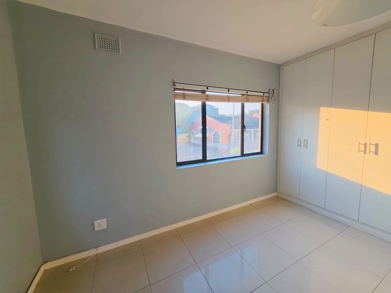 A bright, empty bedroom featuring neutral tiled flooring, built-in cupboards, and a window with natural light.