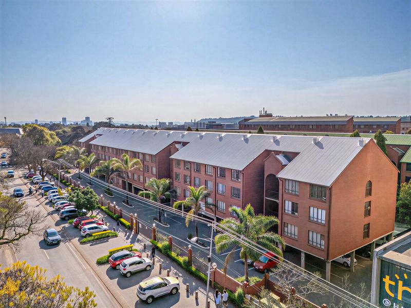 Aerial view of a multi-story brick apartment complex featuring a metal roof, paved parking facilities, and established palm tree landscaping.