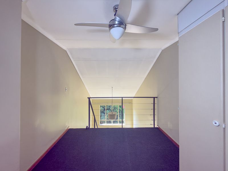 An open mezzanine hallway featuring a ceiling fan, metal balustrade, and built-in storage, overlooking the lower level through a large window.