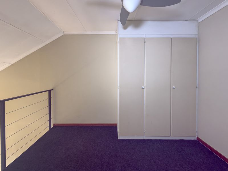 An empty bedroom featuring built-in cupboards, a ceiling fan, and a metal balustrade overlooking the lower level.