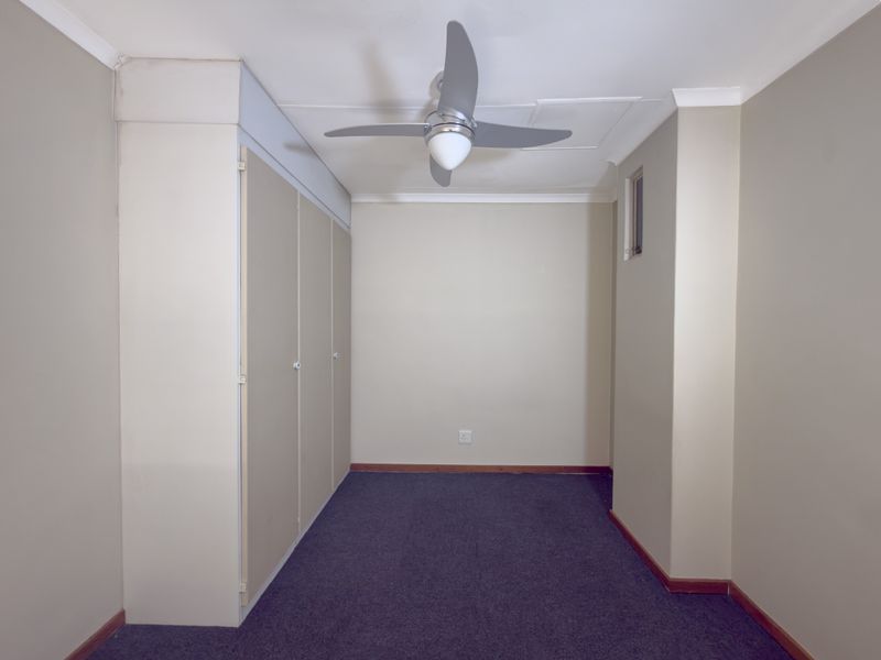An empty bedroom featuring built-in cupboards, a ceiling fan, and carpeted flooring, providing a neutral blank canvas for personalization.