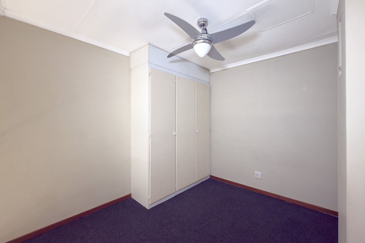 A clean, empty bedroom featuring neutral walls, dark carpeting, a built-in wardrobe, and a ceiling fan.