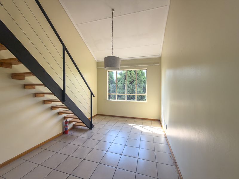 An empty living area featuring tiled flooring, a staircase with a metal balustrade, and a large window providing natural light.