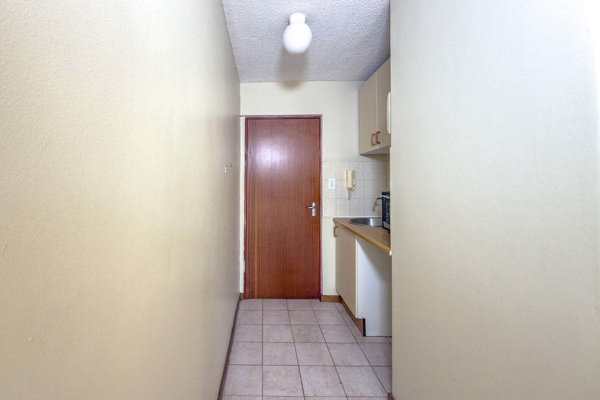A compact kitchenette featuring basic built-in cabinetry, a stainless steel sink, and tiled flooring, presenting an opportunity for modernization and renovation.