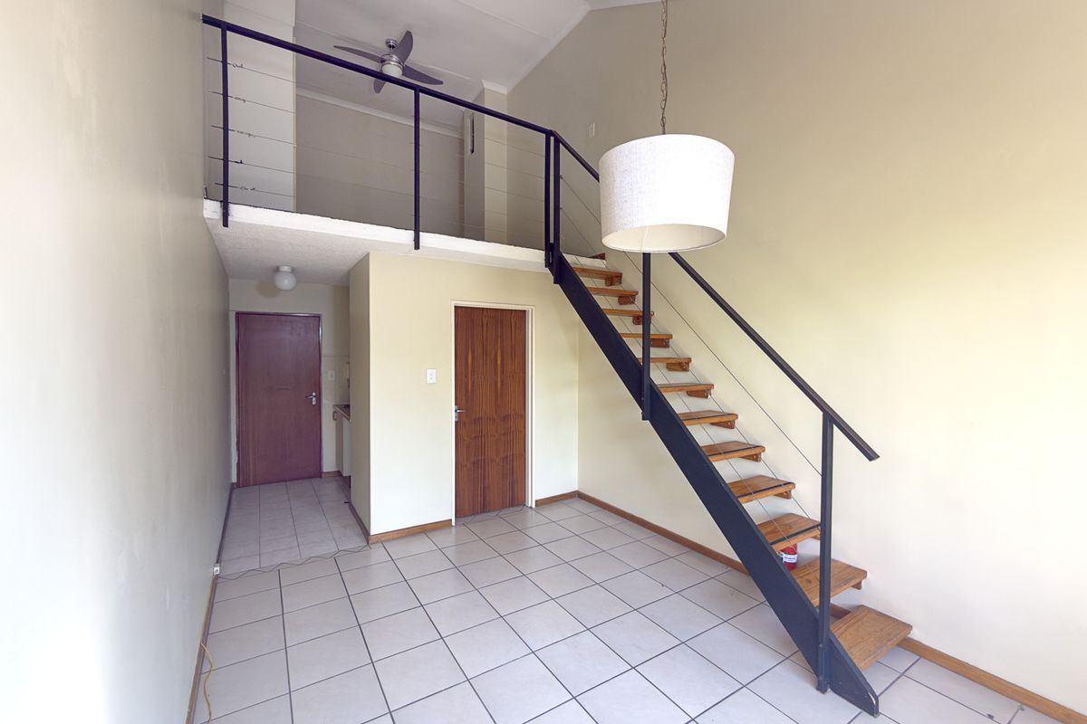 An open-plan living area featuring a mezzanine level, a modern staircase with metal railings, tiled flooring, and a vaulted ceiling.