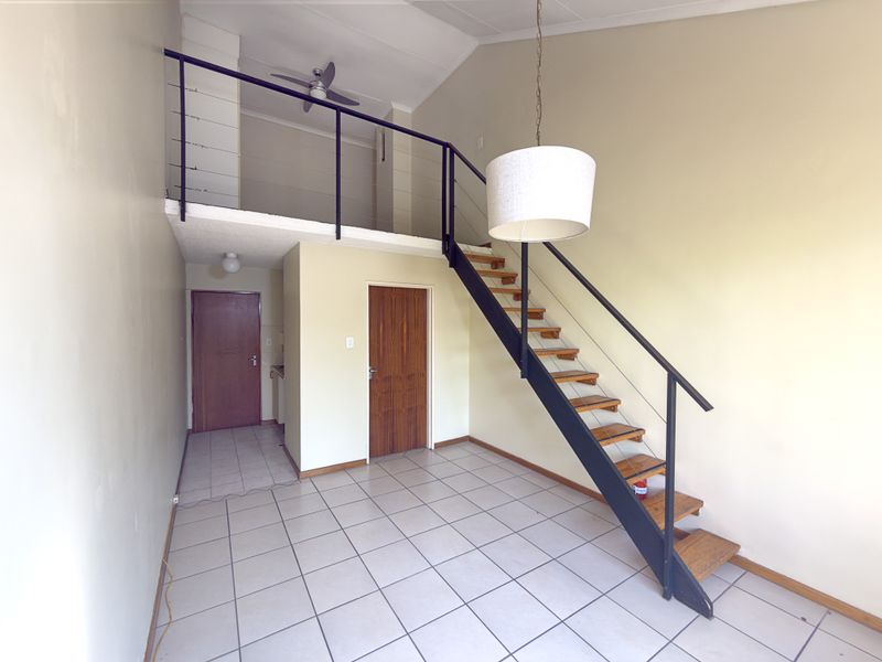 An open-plan living area featuring a mezzanine level, a modern staircase with metal railings, tiled flooring, and a vaulted ceiling.